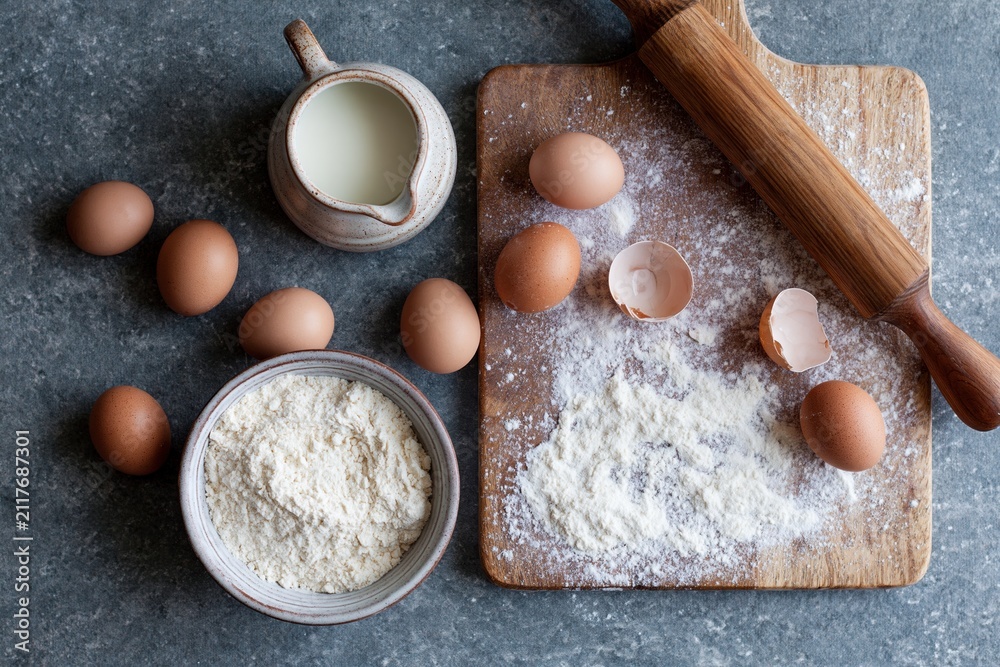 Fototapeta premium The Baking Essentials: Eggs, Flour, Milk and Rolling Pin on a Rustic Board