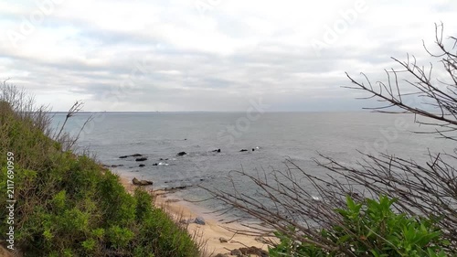 A serene coastal landscape featuring a sandy beach, calm ocean, and rocky shoreline under a cloudy sky. Nobody is present. This evocative scene conveys tranquility, perfect for travel concepts.