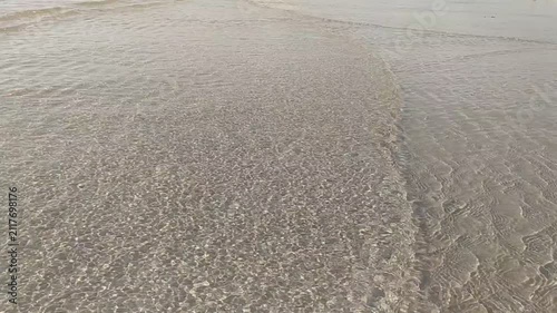 A serene, minimalist view of crystalclear ocean water washing over sandy shores, with nobody present. The tranquil ripples evoke peace and relaxation, perfect for travel or wellness backgrounds.