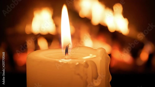 Warm single white candle flame burning brightly against a cozy blurry fireplace background