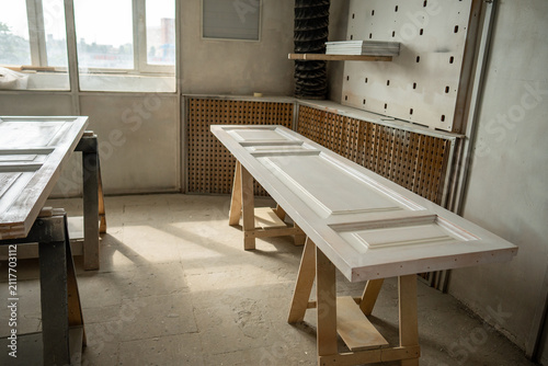 Painting area in restoration workshop, reconstructed antique wooden doors drying out after painting, professional drying zone in woodworking studio, vintage doors lying on construction sawhorses.