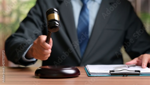 Obraz na plátne Male judge wearing dark suit holding wooden gavel over sound block near legal paper document clipboard inside courtroom office setting before official justice proceeding trial decision