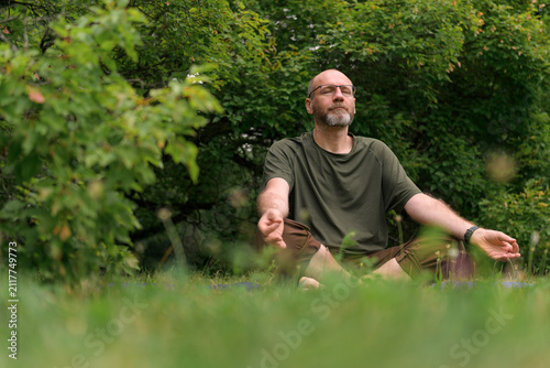 Person meditating cross‑legged on grass in a forest setting