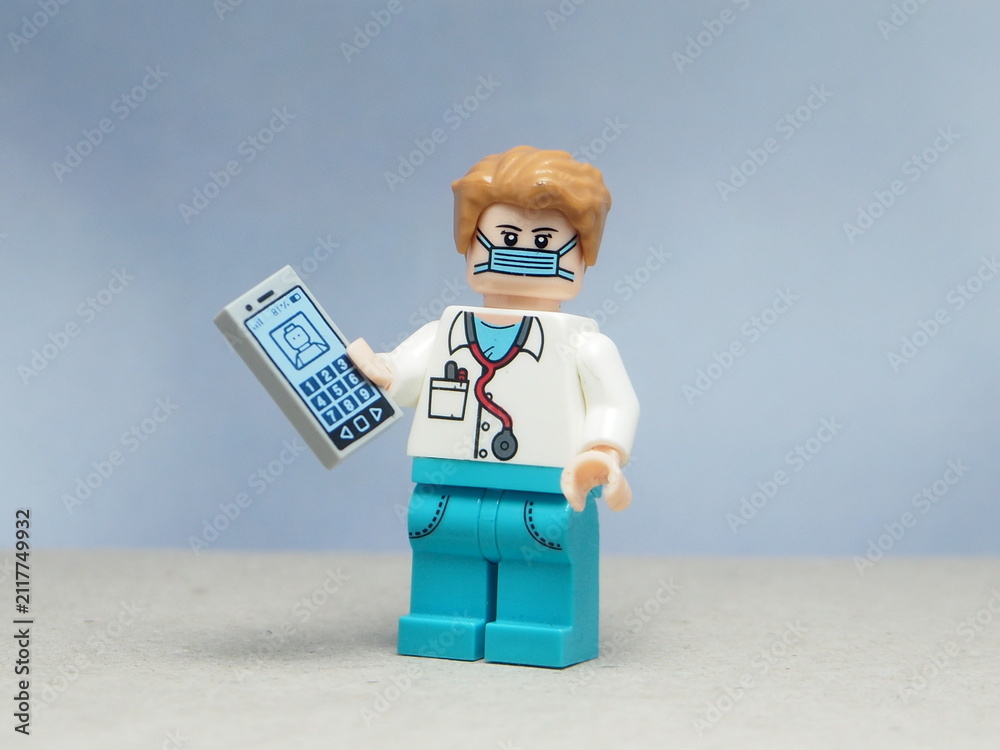 Naklejka premium Indonesia - May 16, 2025 : Mini toy of action figure at table with blurred background. Miniature photography concept design. Minifigure of professional doctor character hold the smartphone at hospital