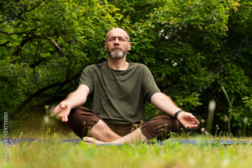 Person meditating cross‑legged on a mat in a green park