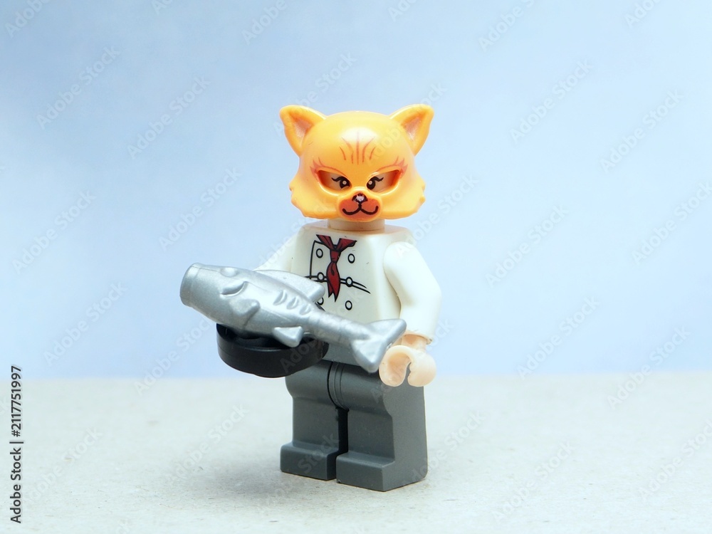 Fototapeta premium Indonesia - May 16, 2025 : Mini toy of action figure at table with blurred background. Miniature photography concept design. Minifigure of orange cat character wearing chef costume with pan and fish.