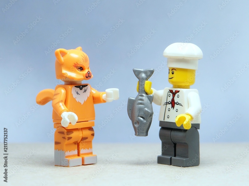 Fototapeta premium Indonesia - May 16, 2025 : Mini toy of action figure at table with blurred background. Miniature photography concept design. Minifigure of chef and cat guy character with fresh fish. Eating fish.