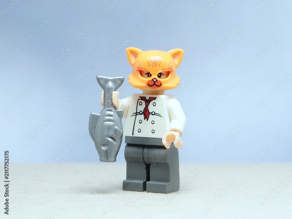 Fototapeta premium Indonesia - May 16, 2025 : Mini toy of action figure at table with blurred background. Miniature photography concept design. Minifigure of orange cat character wearing chef costume with pan and fish.