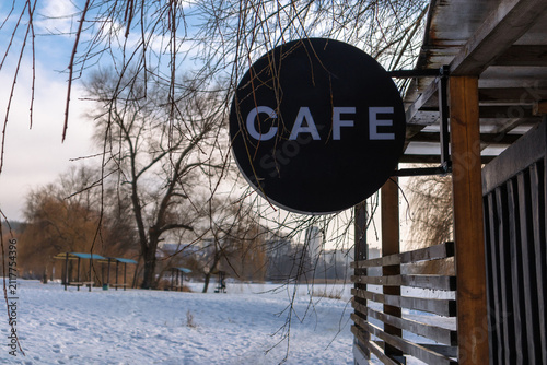 Black round cafe sign on wooden terrace in winter landscape