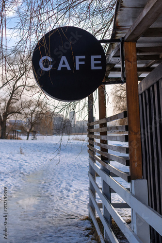 Black round CAFE sign on wooden veranda by the lake in winter
