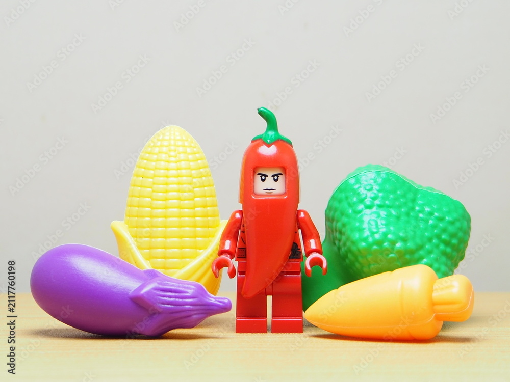 Fototapeta premium Indonesia - February 10, 2026 : Mini toy of action figure at outdoor with blur background. Miniature photography concept design. Minifigure of red chilli guy character with various vegetable.