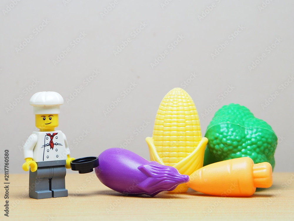 Fototapeta premium Indonesia - February 10, 2026 : Mini toy of action figure at outdoor with blur background. Miniature photography concept design. Minifigure of chef character with eggplant, corn, broccoli and carrot.