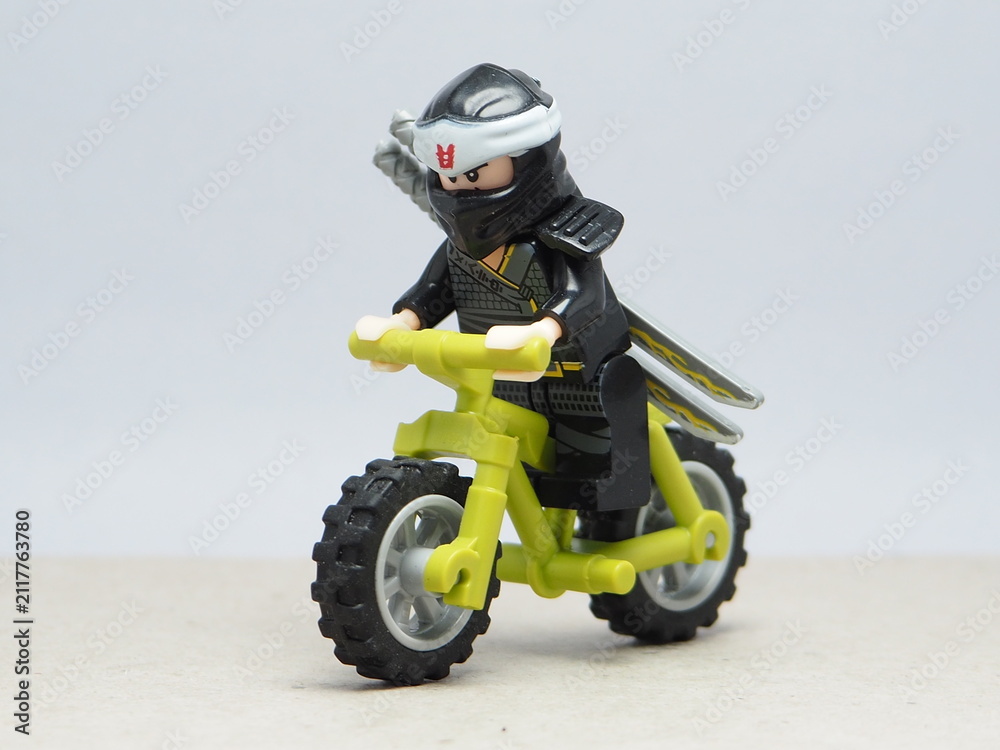Fototapeta premium Indonesia - December 1, 2025 : Mini toy of action figure at outdoor with blurred background. Miniature photography concept design. Minifigure of Ninja Go character riding the mountain bike at outdoor