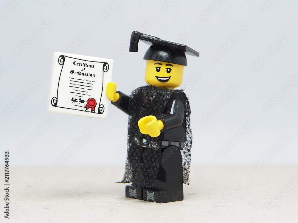 Obraz premium Indonesia - November 24, 2025 : Mini toy of action figure at table with blurred background. Miniature photography concept design. Minifigure of student with graduation gown, cap and certificate.