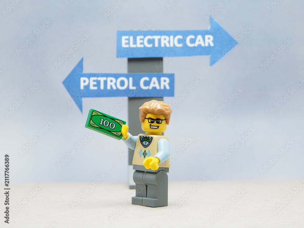 Fototapeta premium Indonesia - April 14, 2025 : Mini toy of action figure at table with blur background. MIniature photography concept design. Minifigure of people character with roadsign. Electrical Car vs Petrol Car.