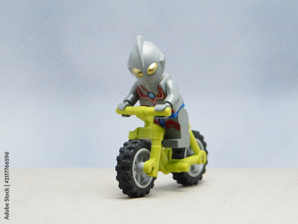 Fototapeta premium Indonesia - April 14, 2025 : Mini toy of action figure at table with blurred background. Toy photography concept design. Minifigure of Ultra Man character from japanese fiction film riding bicycle.