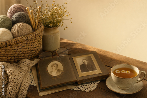Woven basket with yarn, knitting needles, vintage photo album and chamomile tea, nostalgic hobby and storytelling concept