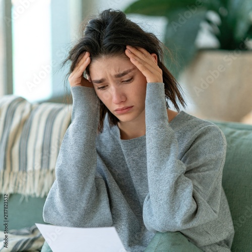 Upset woman reading heartbreaking letter at home holding head with sad expression for article background and mental health awareness banner
