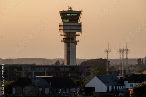 The air traffic control tower of Brussels Airport stands above the surrounding buildings in Belgium in warm golden hour light, the centre of airport operations.
