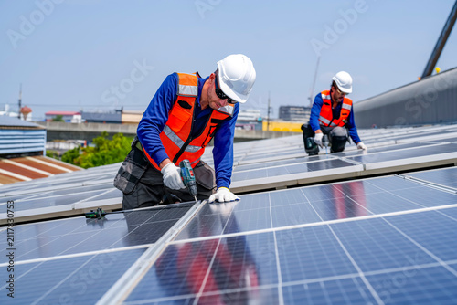 Workers install solar panels on a rooftop in a city during a sunny day while using tools to secure the panels