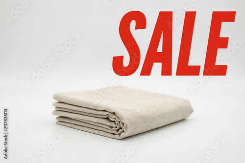 A neat stack of light beige natural linen fabric cloth textiles for clothing home decor or craft projects with a prominent bright red SALE sign indicating a discount promotion opportunity