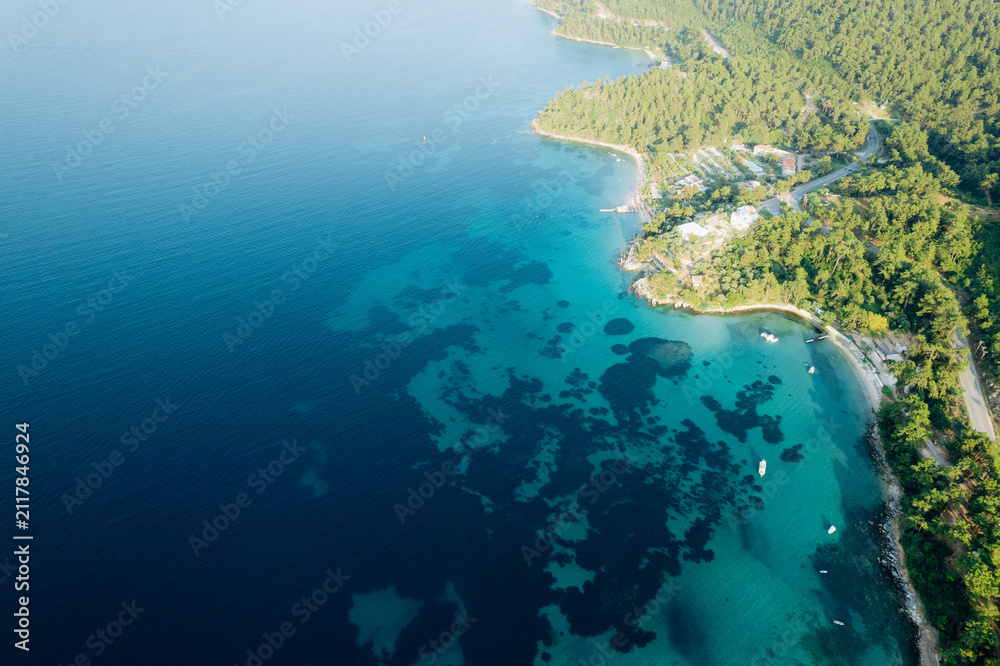 Fototapeta premium Aerial summer landscape of a turquoise lagoon on Thassos Island, Greece, showing crystal clear water, beach, swimmers, paddleboards and rocky coastline. 