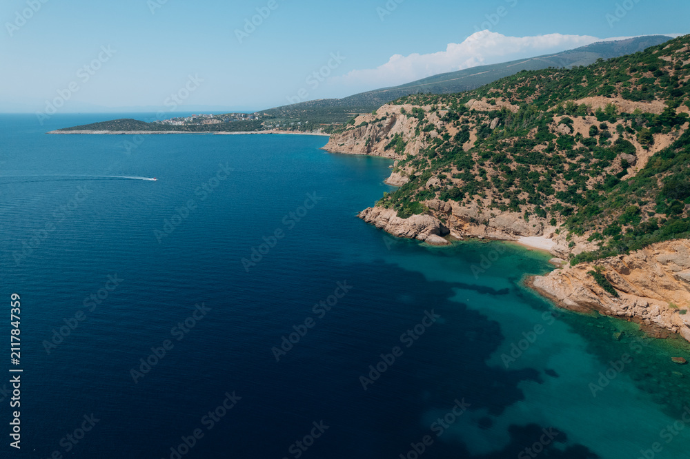 Naklejka premium Aerial drone view of a crystal clear turquoise bay on Thassos Island, Greece, with swimmers, paddleboards and a sandy beach surrounded by rocky coastline on a sunny summer day. 