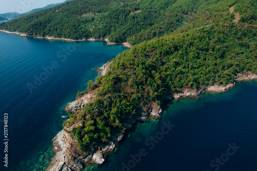 Aerial summer landscape of a turquoise lagoon on Thassos Island, Greece, showing crystal clear water, beach, swimmers, paddleboards and rocky coastline.	
