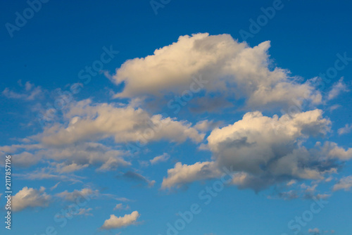 Fotografie Fluffy white and golden clouds float across a deep blue sky in the evening sunlight