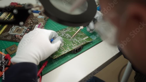 Close-up an electronics technician soldering a printed circuit board during electronic equipment repair. Precision engineering, PCB diagnostics, right to repair. Technology and electronics service.
