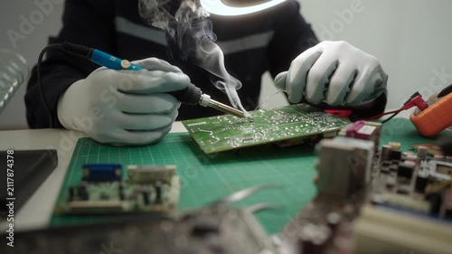 Electronics technician soldering a printed circuit board during electronic equipment repair. Precision engineering, PCB diagnostics, right to repair. Technology and electronics service.
