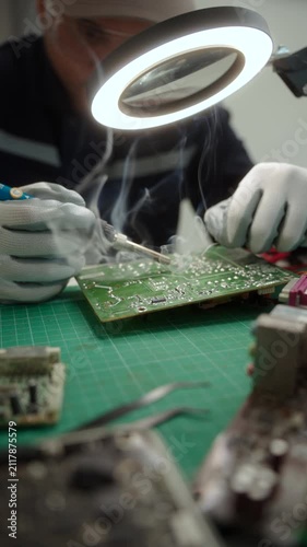Electronics technician soldering a printed circuit board during electronic equipment repair. Precision engineering, PCB diagnostics, right to repair. Technology and electronics service.
