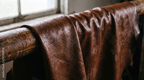 Wet brown leather hide hanging on a wooden drying rack in a tannery