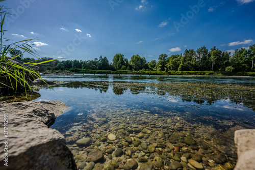 Klare Wasseroberfläche mit Steinen am Ufer eines Flusses an einem sonnigen Tag im Sommer