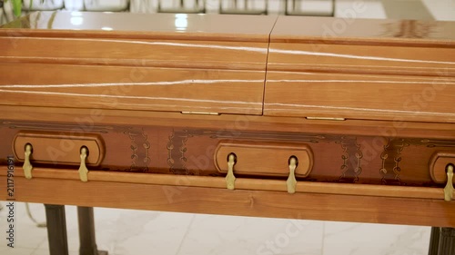 Closed wooden coffin in a bright funeral home or chapel. Solemn farewell ceremony setup with white floral arrangements, empty chairs, and a religious icon.