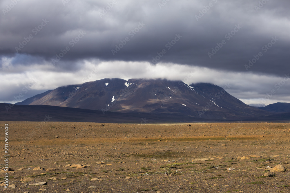 Fototapeta premium Barren volcanic mountain stands beneath heavy storm cloud in the Icelandic Highlands