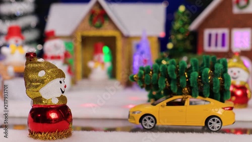Against the backdrop of a small Christmas village, a yellow car drives up to a snowman
