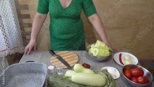 A woman in a green dress is preparing to cook in the kitchen close-up, Culinary process, a woman stands at the table with vegetables and kitchen utensils