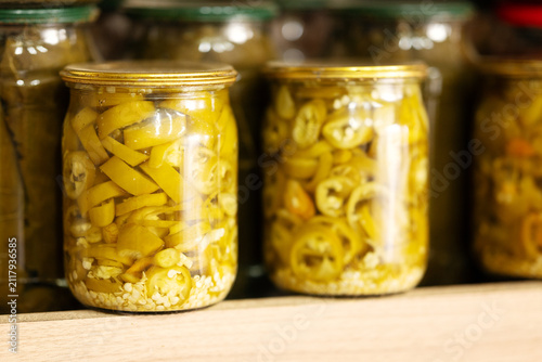 Home canned pickled sliced chili peppers in glass jars on shelf. Preserved hot jalapeno peppers for culinary recipes, food industry, and retail grocery market.
