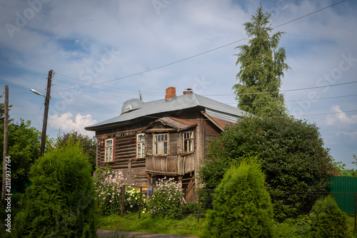 Kimry, Tver Region, Russia, 15 July 2026 Old wooden log house with carved trim and blooming hollyhocks,