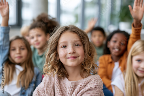 Bright classroom scene with smiling children. Children raise hands eagerly. Focus on girl in soft sweater, centered. Warm light bathes the group. Ideal for education or learning themes