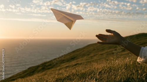 Creating Paper Airplane and Releasing It Into the Wind Over Grassy Hilltop by the Ocean at Sunset