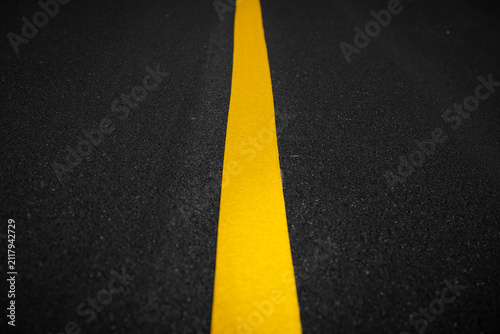 A close-up view of a bright yellow dividing line on a dark asphalt road surface