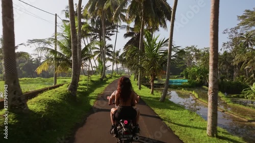 Aerial view of couple riding a scooter on a road surrounded by palm trees and rice fields