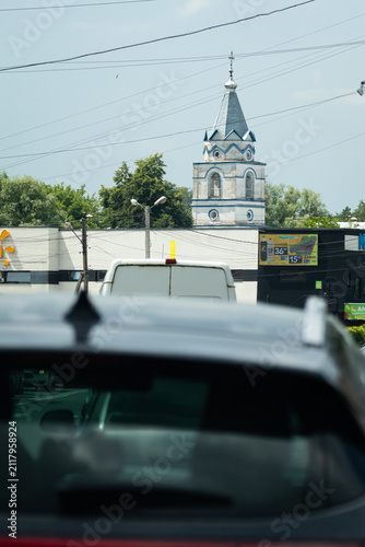 Fotografía Vehicles bunch along a city street beneath a web of wires while a distant spire rises
