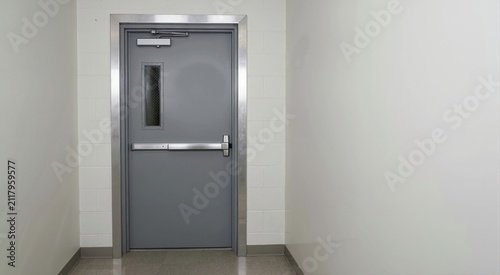 Grey metal emergency exit door with a push bar. Commercial building safety escape route in a white cinderblock hallway