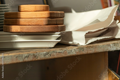 Wooden trays stacked on a table next to ceramic plates in a kitchen setting