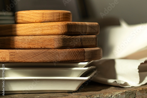 Wooden trays stacked on a table next to ceramic plates in a kitchen setting
