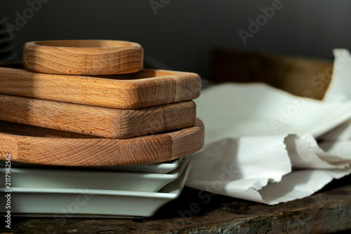 Wooden trays stacked on a table next to ceramic plates in a kitchen setting