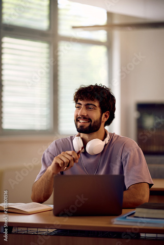 Happy male student using laptop while studying at university classroom.